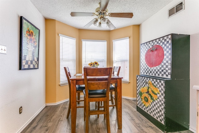 dining space with a textured ceiling, wood finished floors, visible vents, and baseboards