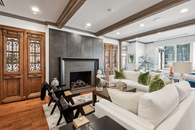 living room with beam ceiling, a fireplace, visible vents, ornamental molding, and light wood-type flooring