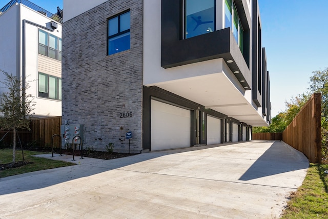 view of property exterior with brick siding, stucco siding, fence, a garage, and driveway