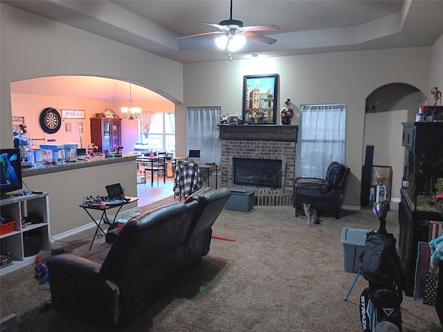 carpeted living room featuring ceiling fan with notable chandelier, a raised ceiling, a fireplace, and arched walkways