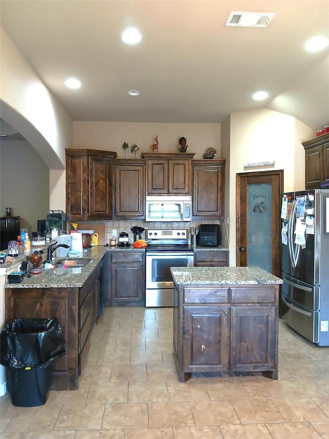 kitchen featuring light stone countertops, visible vents, dark brown cabinets, appliances with stainless steel finishes, and tasteful backsplash