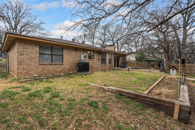 rear view of house featuring brick siding, a yard, central AC unit, fence, and a garden