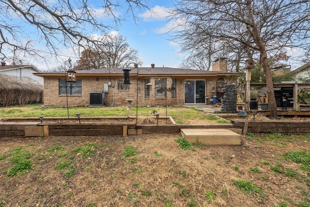 back of property featuring a vegetable garden, a chimney, cooling unit, a yard, and brick siding