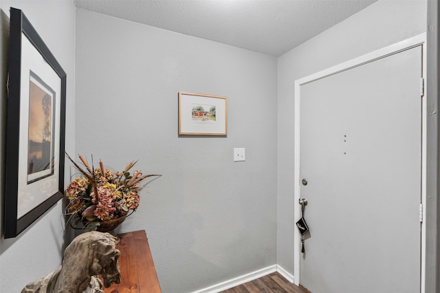 foyer featuring a textured ceiling, baseboards, and wood finished floors