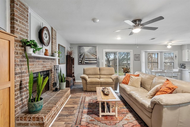 living room with a ceiling fan, a fireplace, visible vents, and wood finished floors