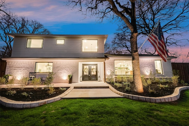 front of house at dusk featuring a patio area, fence, french doors, and a lawn