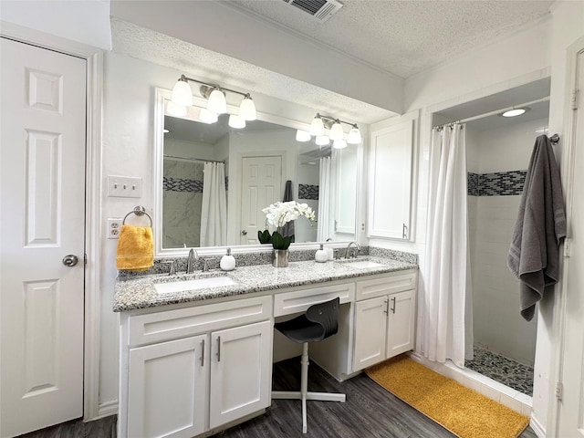 bathroom featuring a sink, a tile shower, a textured ceiling, and visible vents