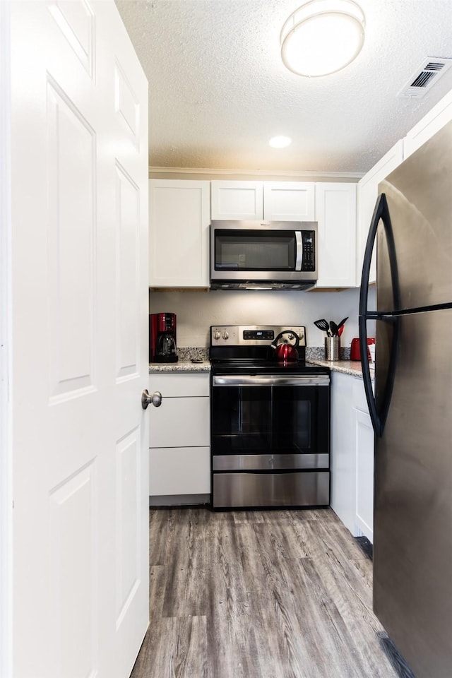 kitchen featuring stainless steel appliances, wood finished floors, visible vents, and white cabinetry