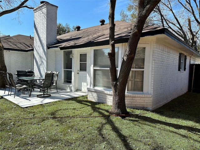 rear view of property featuring a chimney, roof with shingles, a lawn, a patio area, and brick siding