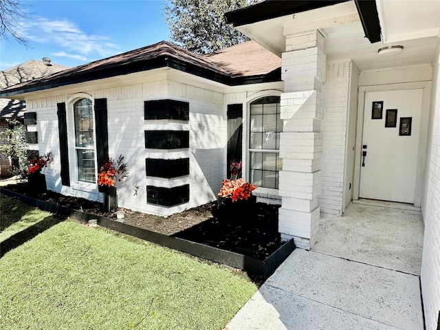 doorway to property with a shingled roof and brick siding