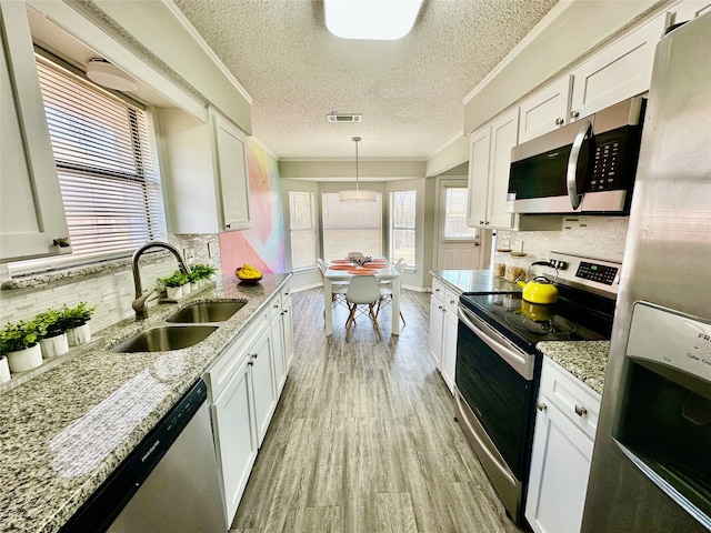 kitchen featuring light wood finished floors, visible vents, appliances with stainless steel finishes, ornamental molding, and a sink