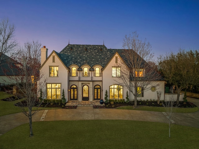 french country inspired facade with curved driveway, a front yard, stucco siding, french doors, and a chimney