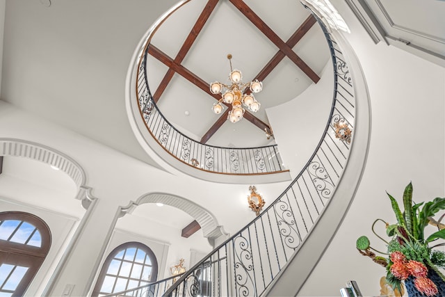 staircase with beamed ceiling, a high ceiling, and a chandelier