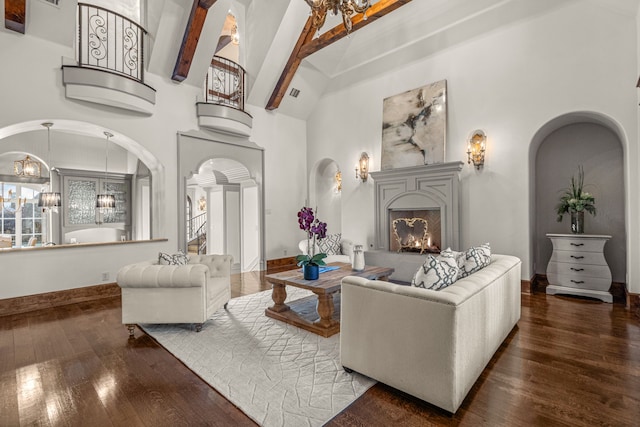 living area featuring a warm lit fireplace, a towering ceiling, arched walkways, a notable chandelier, and wood-type flooring