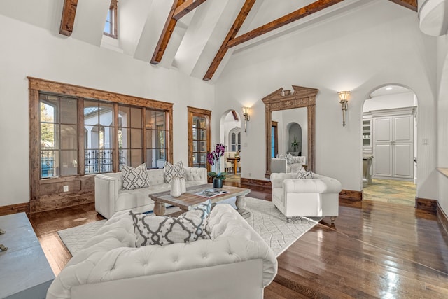 living area featuring baseboards, beam ceiling, wood finished floors, arched walkways, and high vaulted ceiling