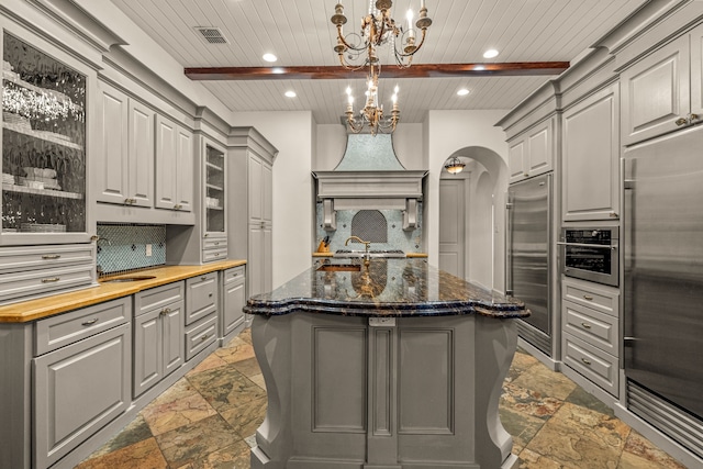 kitchen with stone tile floors, appliances with stainless steel finishes, gray cabinetry, and decorative backsplash