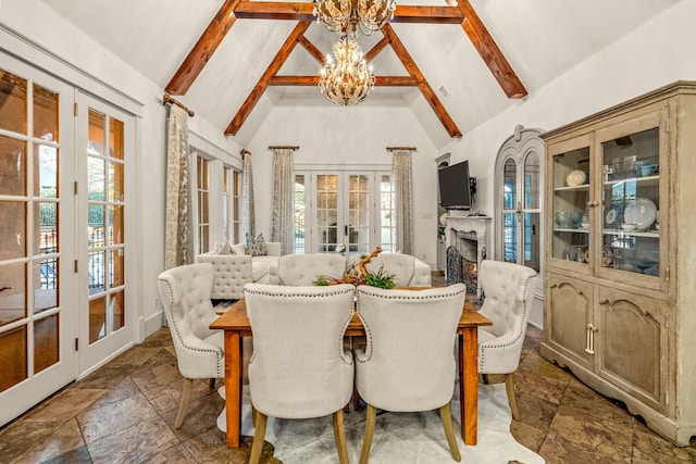 dining space featuring beam ceiling, a warm lit fireplace, stone tile flooring, french doors, and a chandelier