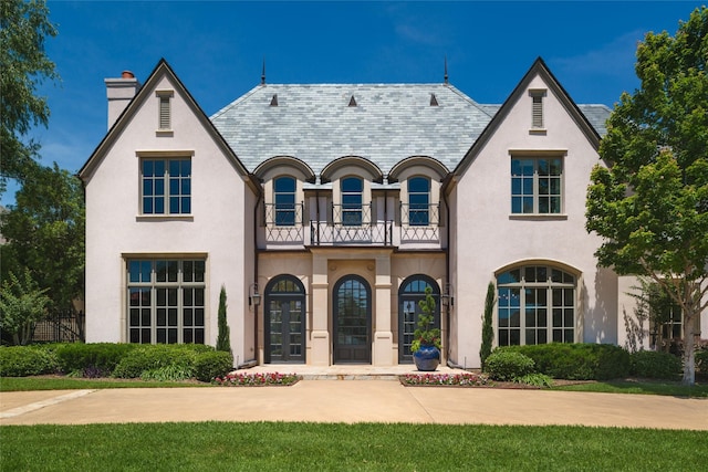 view of front facade with stucco siding, a high end roof, a balcony, and a chimney