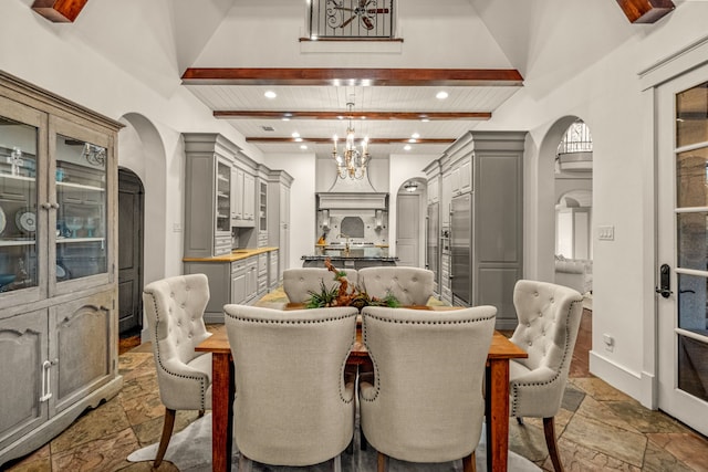 dining room featuring an inviting chandelier, beamed ceiling, arched walkways, and stone tile flooring