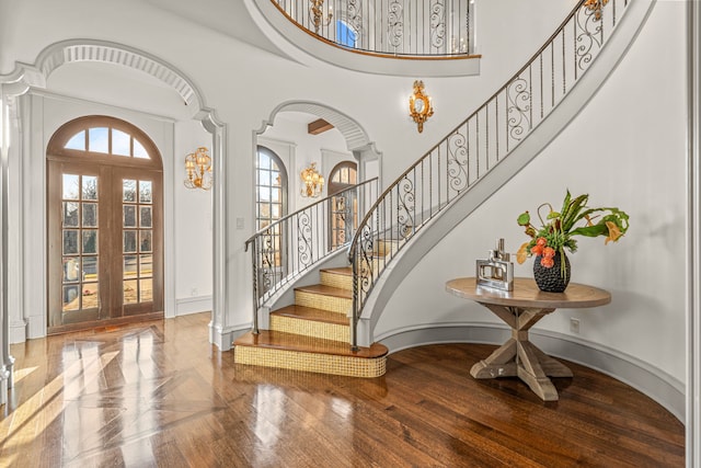 foyer featuring french doors, arched walkways, baseboards, a towering ceiling, and stairs