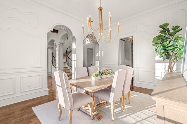 dining space featuring wood finished floors, ornamental molding, stairs, a decorative wall, and a notable chandelier