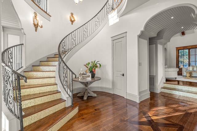 staircase with visible vents, parquet floors, arched walkways, baseboards, and a towering ceiling