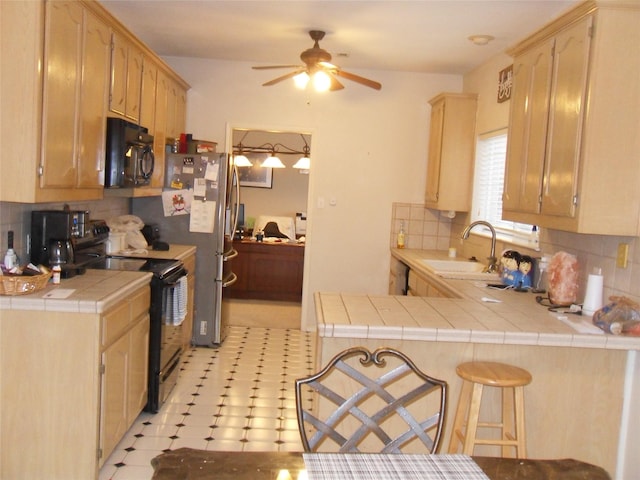 kitchen featuring tasteful backsplash, tile counters, a peninsula, black appliances, and a sink