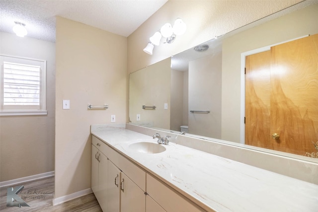 bathroom featuring a textured ceiling, toilet, wood finished floors, vanity, and baseboards