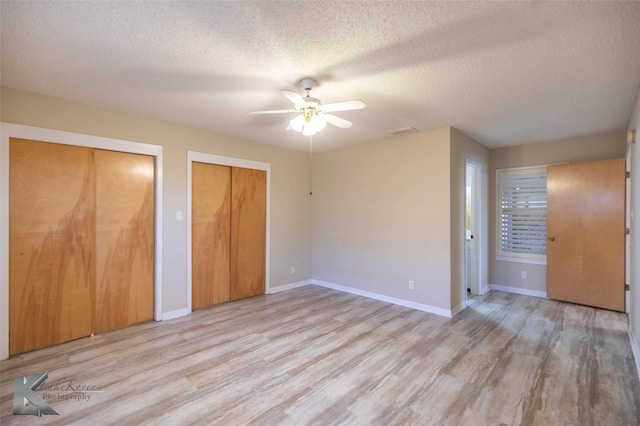 unfurnished bedroom with a textured ceiling, ceiling fan, baseboards, light wood-type flooring, and two closets