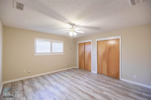 unfurnished bedroom featuring baseboards, light wood-type flooring, visible vents, and multiple closets