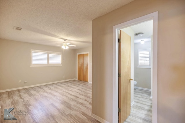 interior space featuring a textured ceiling, a ceiling fan, visible vents, baseboards, and light wood-type flooring