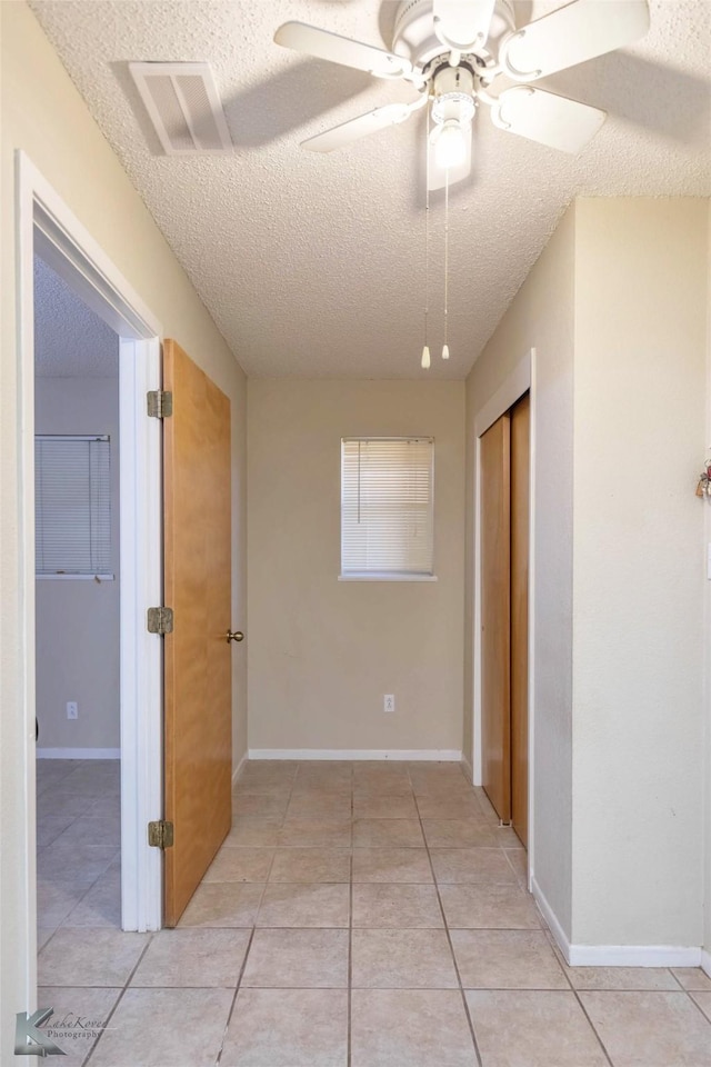 hall featuring light tile patterned floors, a textured ceiling, visible vents, and baseboards