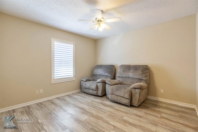 sitting room featuring light wood-type flooring, a ceiling fan, baseboards, and a textured ceiling