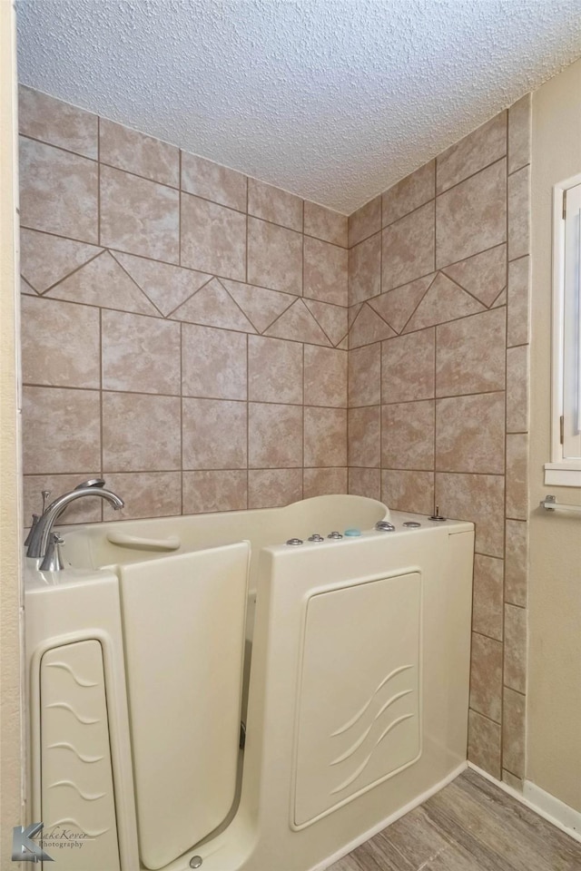 bathroom with a tub to relax in, a textured ceiling, and wood finished floors