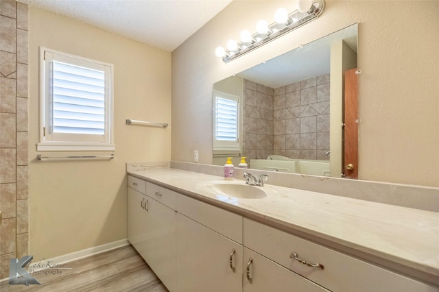 bathroom with a textured ceiling, wood finished floors, vanity, baseboards, and a bath