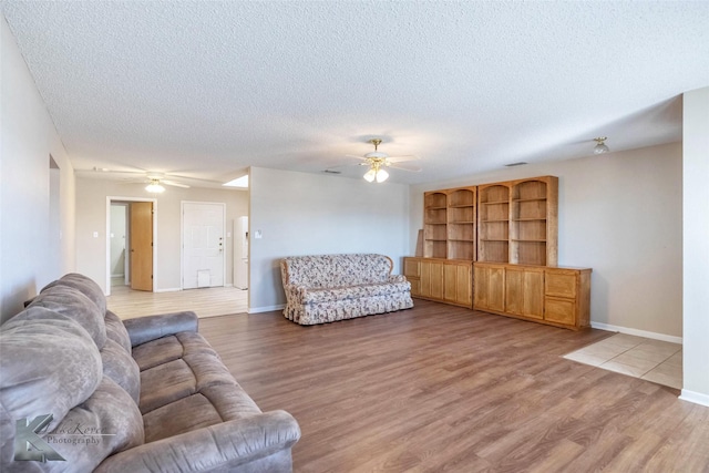 living area featuring a textured ceiling, light wood-type flooring, a ceiling fan, and baseboards