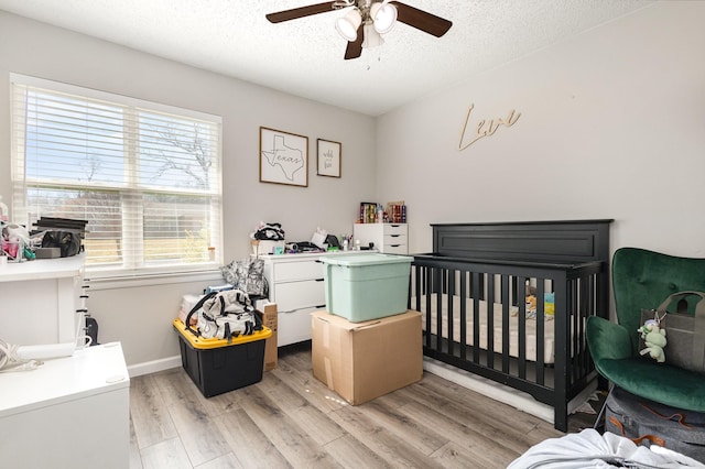 bedroom featuring light wood finished floors, a ceiling fan, a textured ceiling, a nursery area, and baseboards