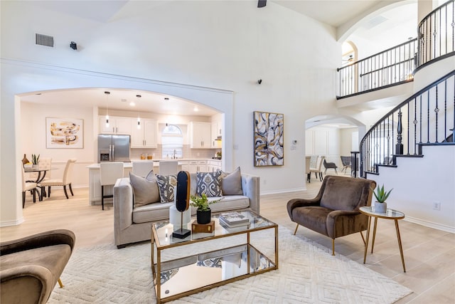 living room with arched walkways, visible vents, stairway, and a high ceiling