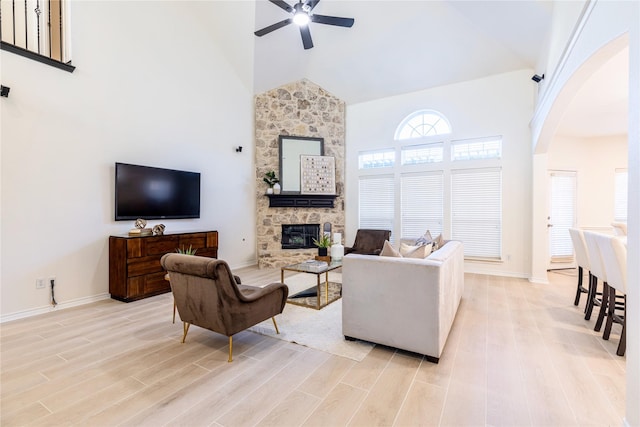 living room with high vaulted ceiling, a ceiling fan, arched walkways, a fireplace, and light wood-type flooring