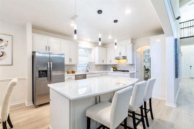 kitchen featuring stainless steel appliances, arched walkways, a sink, a kitchen island, and tasteful backsplash
