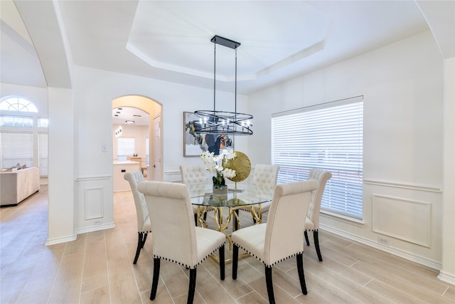 dining room with arched walkways, a chandelier, a raised ceiling, and light wood-style floors