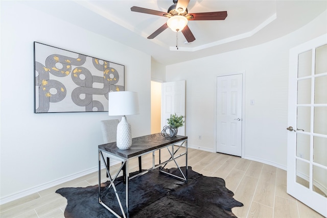 office space featuring a raised ceiling, wood finish floors, ceiling fan, and baseboards