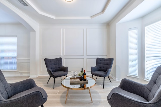 sitting room with a decorative wall, a raised ceiling, arched walkways, and light wood finished floors