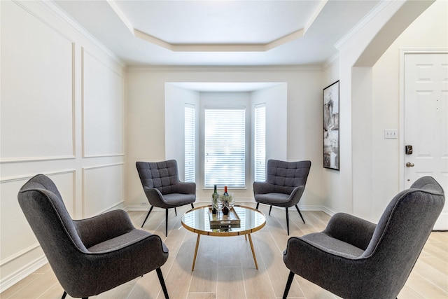 living area featuring a raised ceiling, light wood-style floors, baseboards, and crown molding