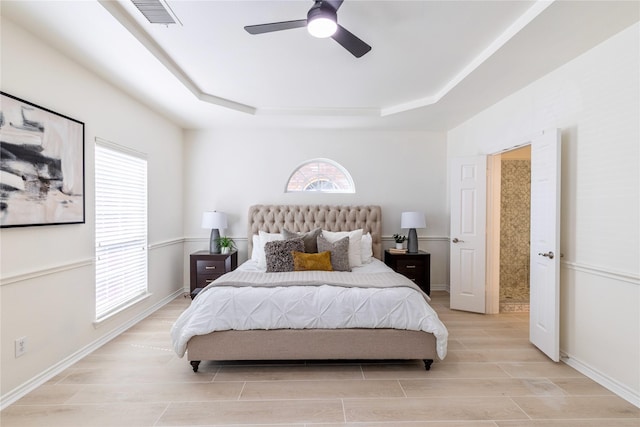 bedroom with a tray ceiling, light wood-type flooring, baseboards, and a ceiling fan