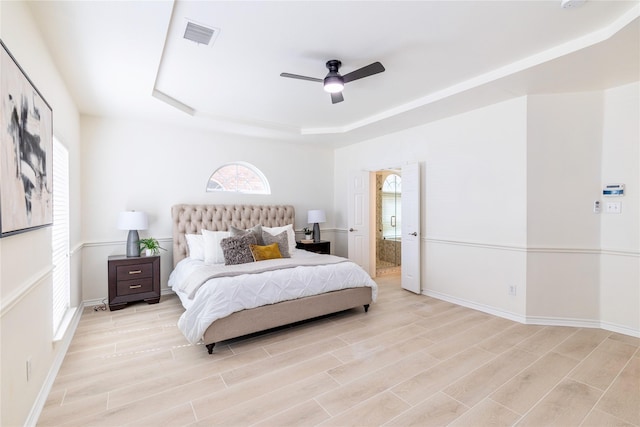 bedroom with a raised ceiling, baseboards, light wood finished floors, and ensuite bath