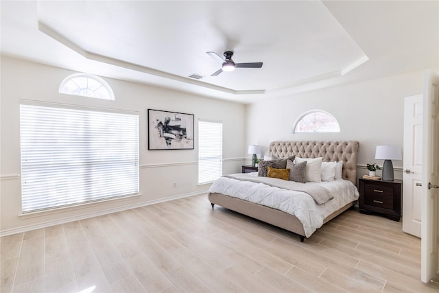 bedroom featuring a raised ceiling, light wood-style flooring, a ceiling fan, and baseboards