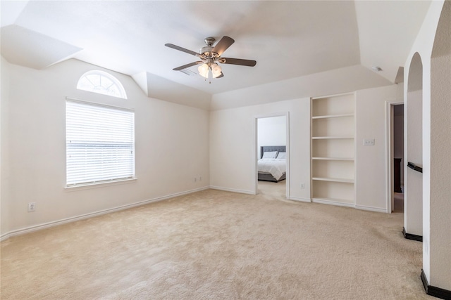 unfurnished bedroom with light carpet, lofted ceiling, baseboards, ceiling fan, and arched walkways