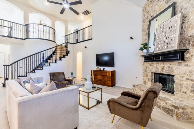 living area featuring a ceiling fan, wood finished floors, stairway, a towering ceiling, and a stone fireplace