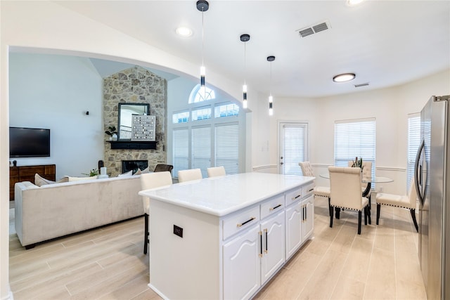 kitchen with freestanding refrigerator, light wood-type flooring, lofted ceiling, a stone fireplace, and white cabinetry